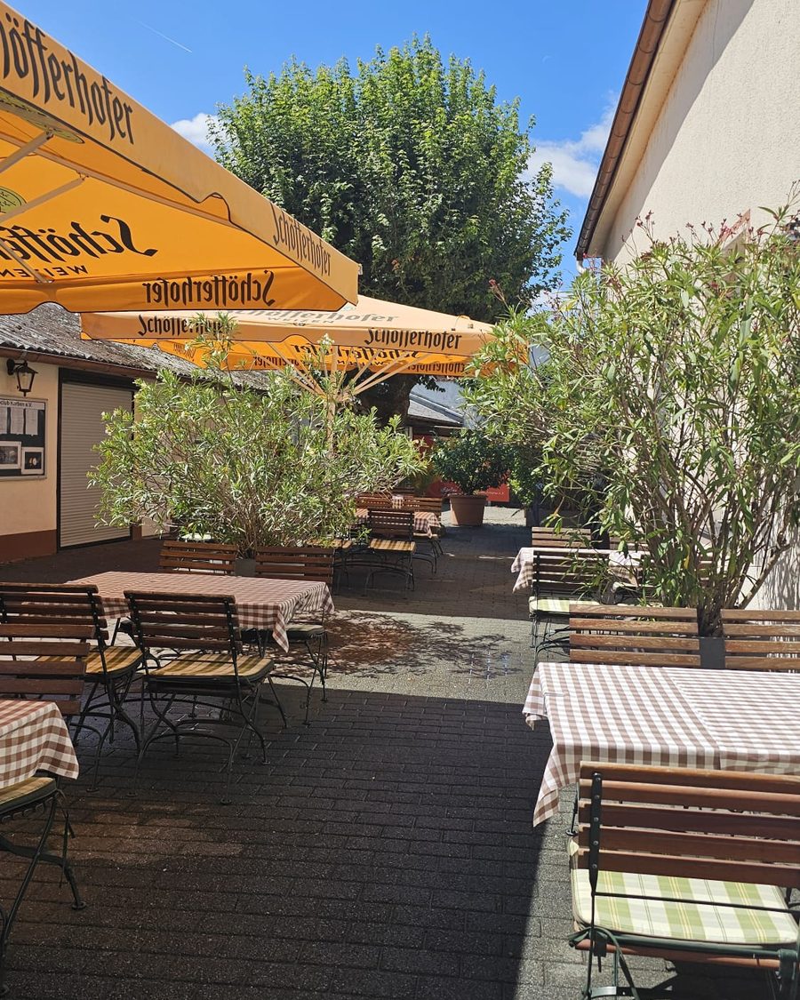 Biergarten mit Bäumen, Sonnenschirmen und blauem Himmel