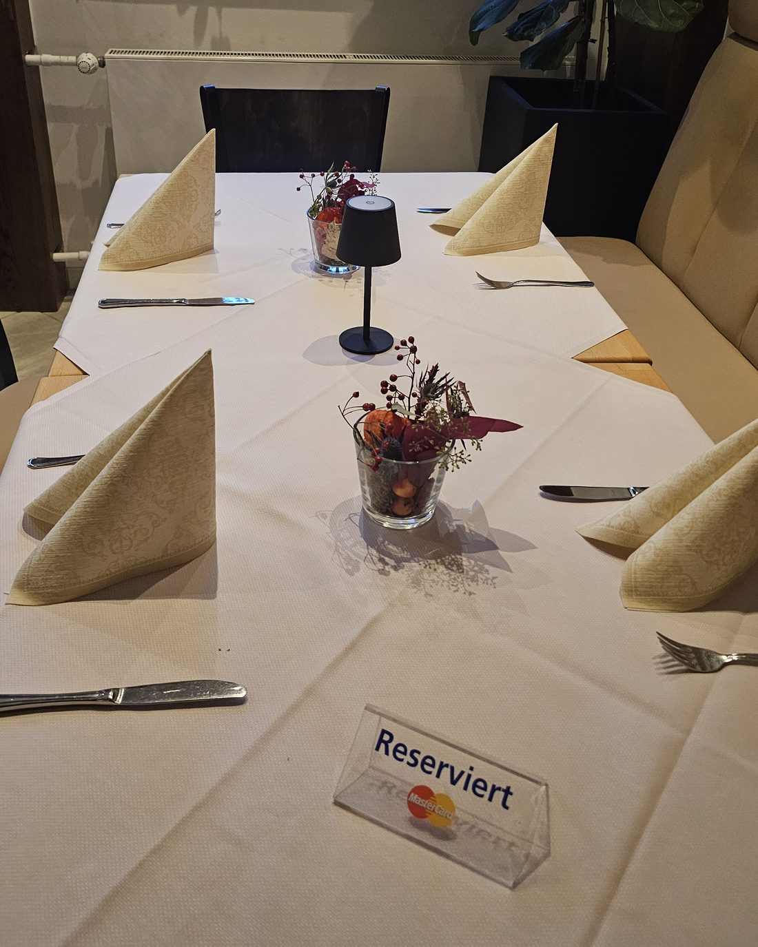Eingedeckter Tisch mit Reserviert-Schild, gefalteten Servietten und kleinem Blumengesteck
