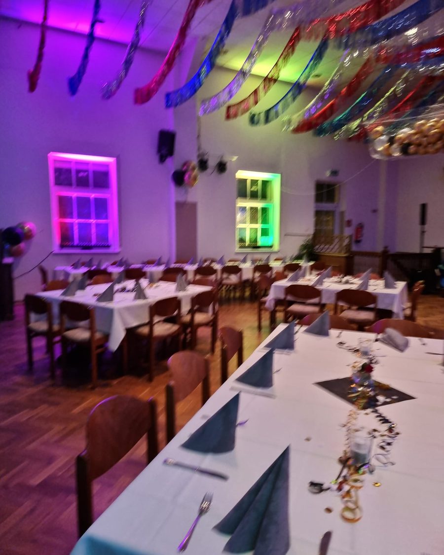 Der große Saal mit bunten Lichtern, Lametta an der Decke und langen, eingedeckten Tischen