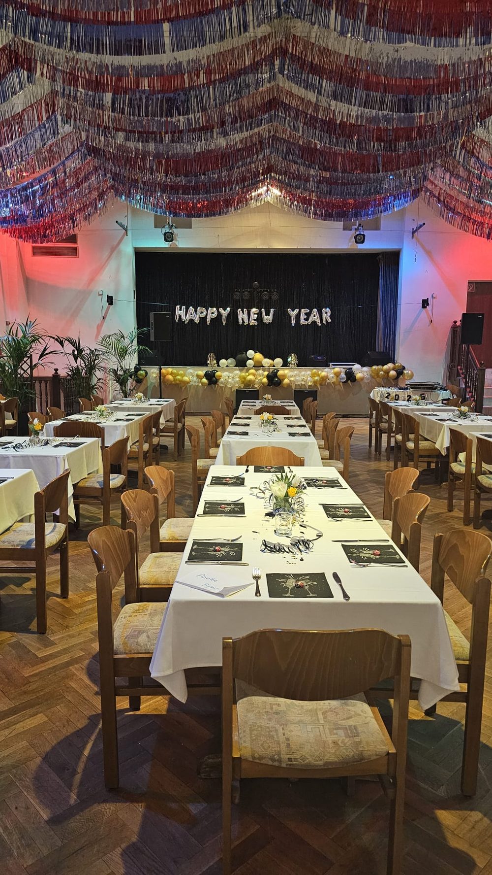 Der große Saal zum Jahreswechsel: lange, weiß eingedeckte Tafeln, Lametta an der Decke und „Happy New Year“ an der Bühne